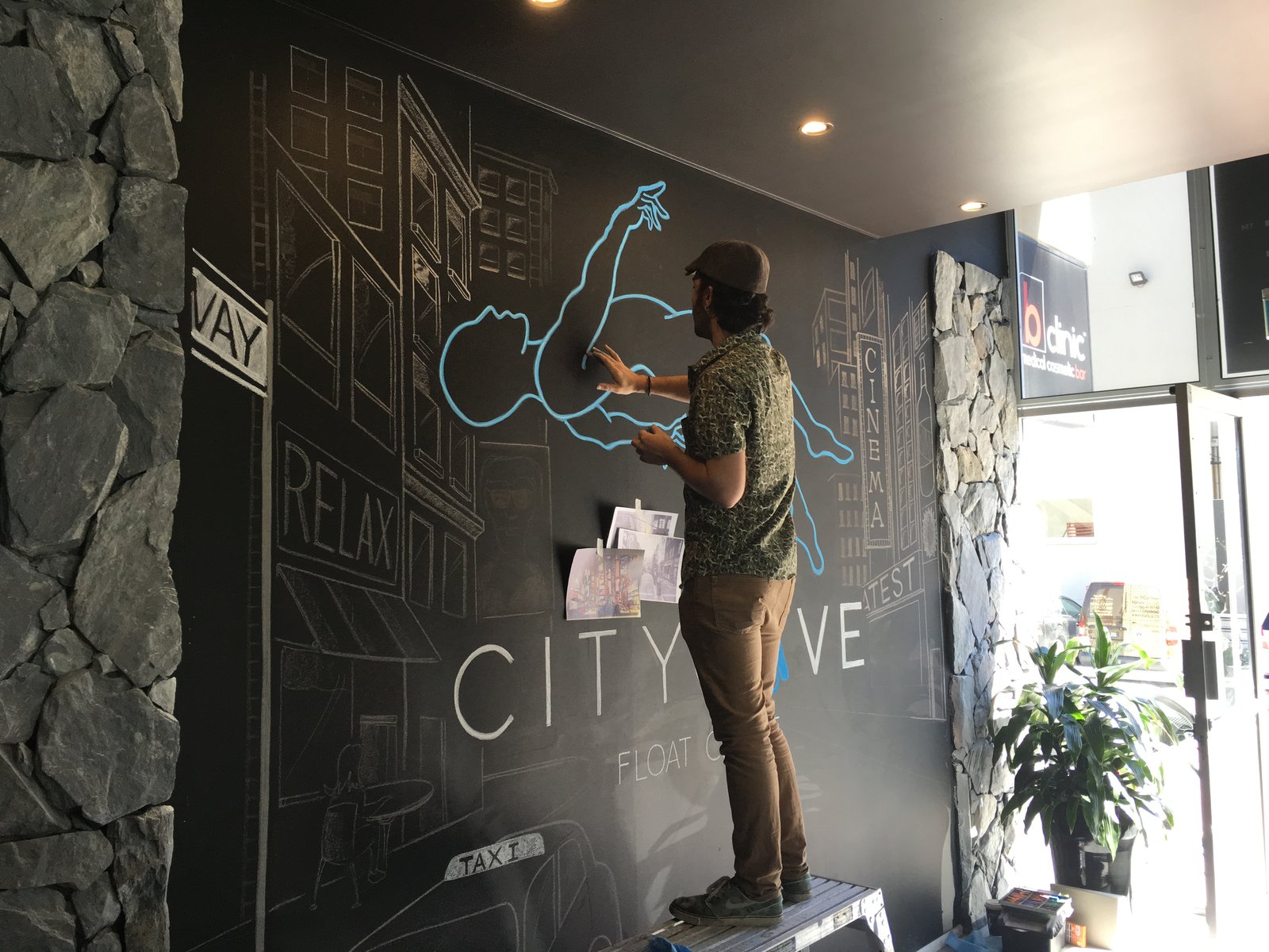 An artist painting a chalk mural of a floating figure over a cityscape inside the first City Cave centre.